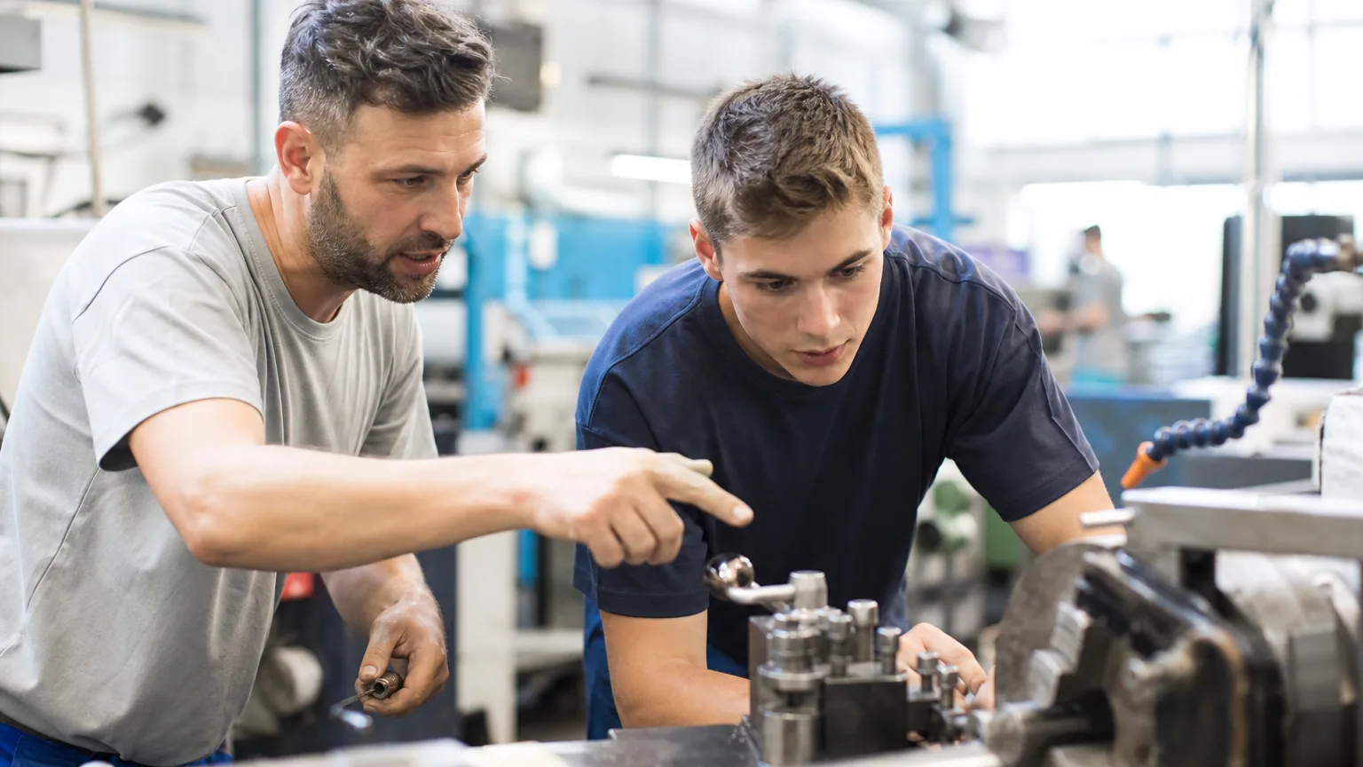 Maître d'apprentissage formant un jeune apprenti sur un poste de travail en entreprise